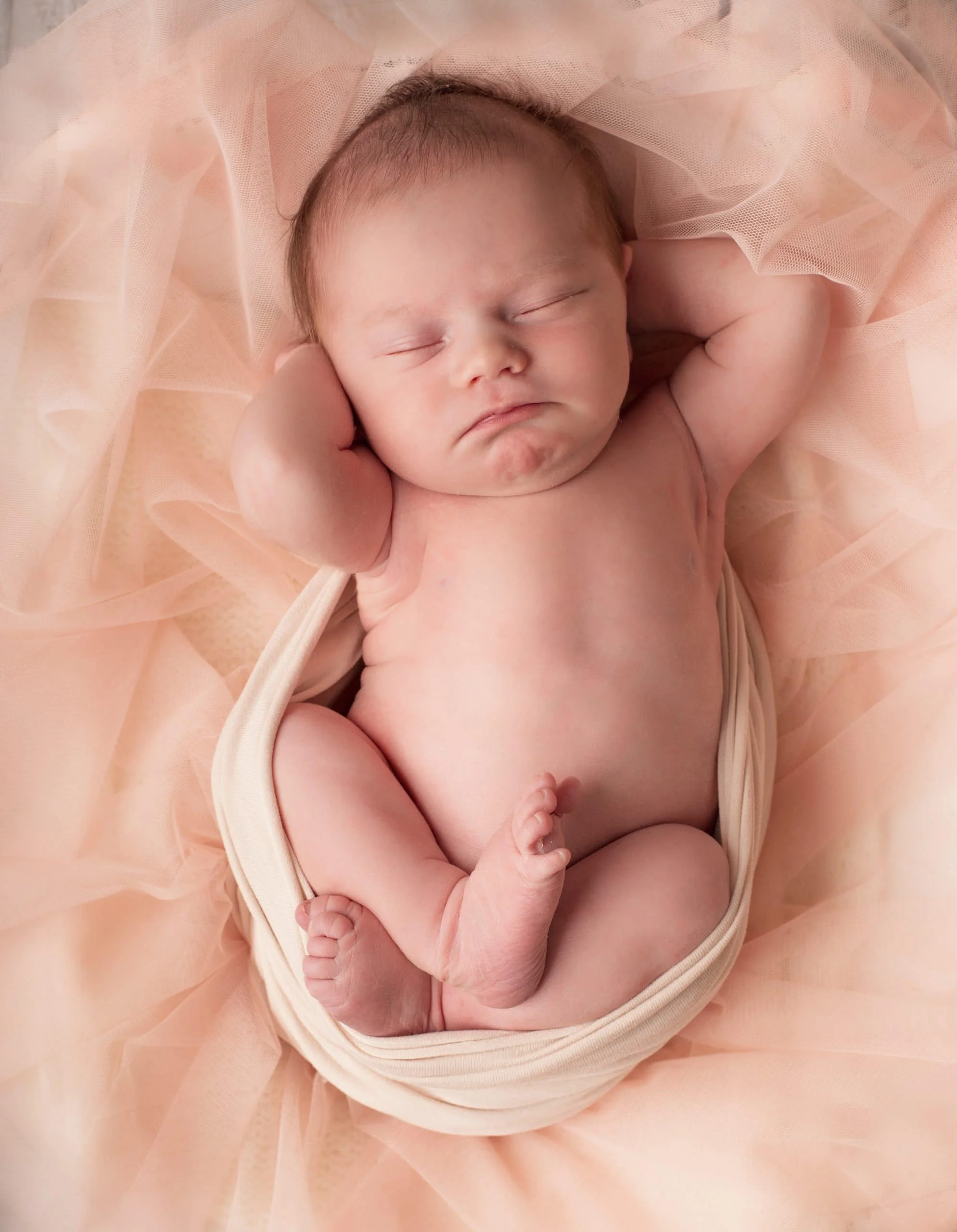 Nydelig nyfødtbaby sovende, omgitt av myk rosa tøy, perfekt for minneverdige fotografier.