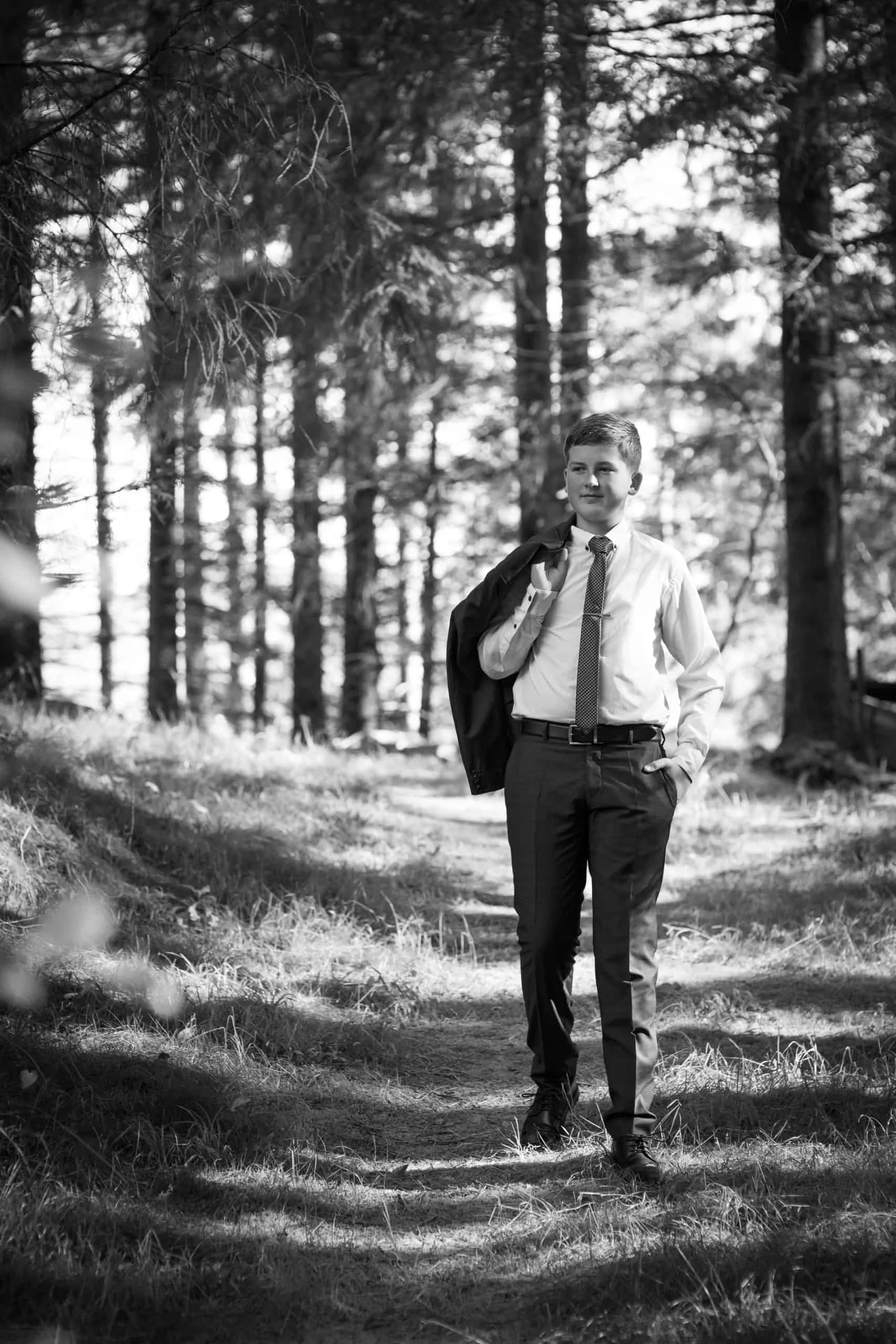 En gutt i dress og slips går gjennom en solfylt skog under en profesjonell fotografering med en dyktig fotograf.