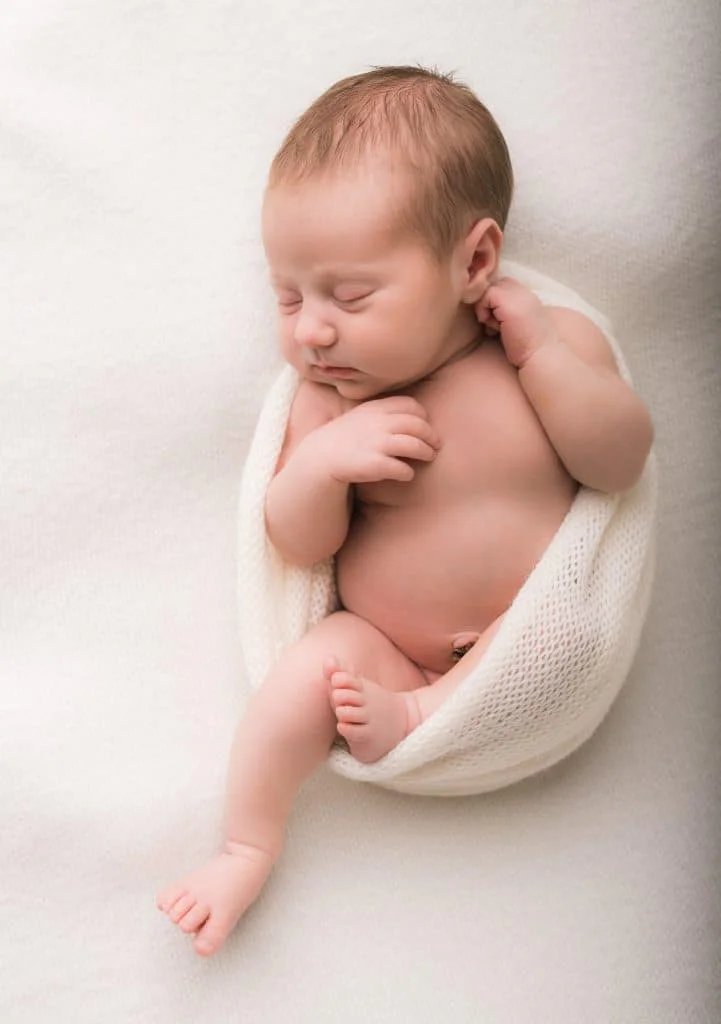 Sovende nyfødt baby i et lyst strikkesjal, profesjonell nyfødtfotografering hos Evig Minne