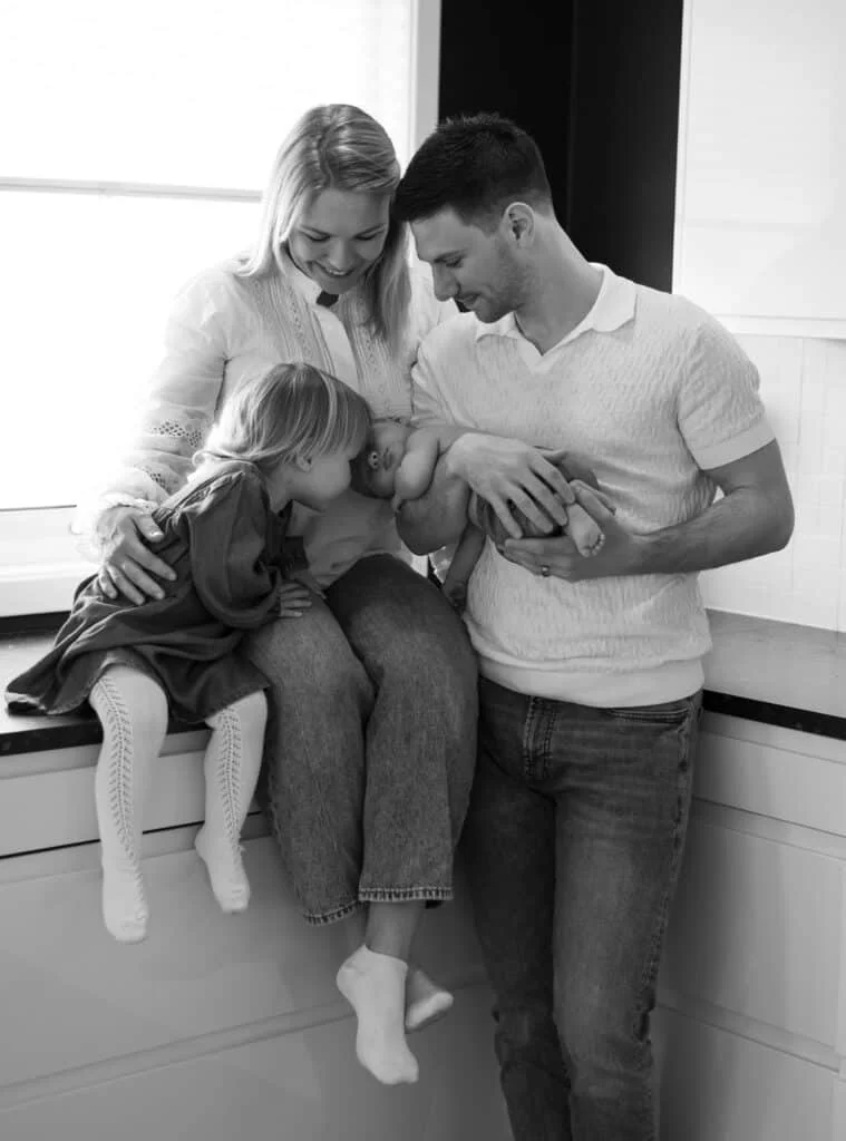Foreldre med sin datter og nyfødte baby i en øm stund under profesjonell nyfødtfotografering hos en babyfotograf.