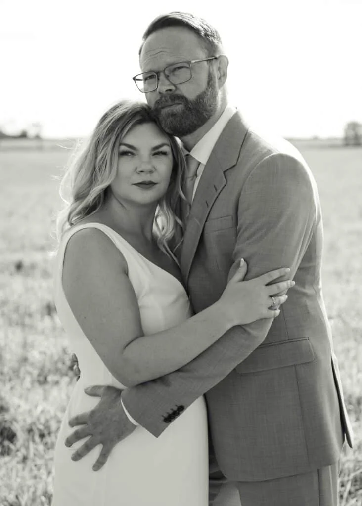 Et par står tett sammen i et åpent landskap under profesjonell fotografering som viser kjærlighet og nærhet.