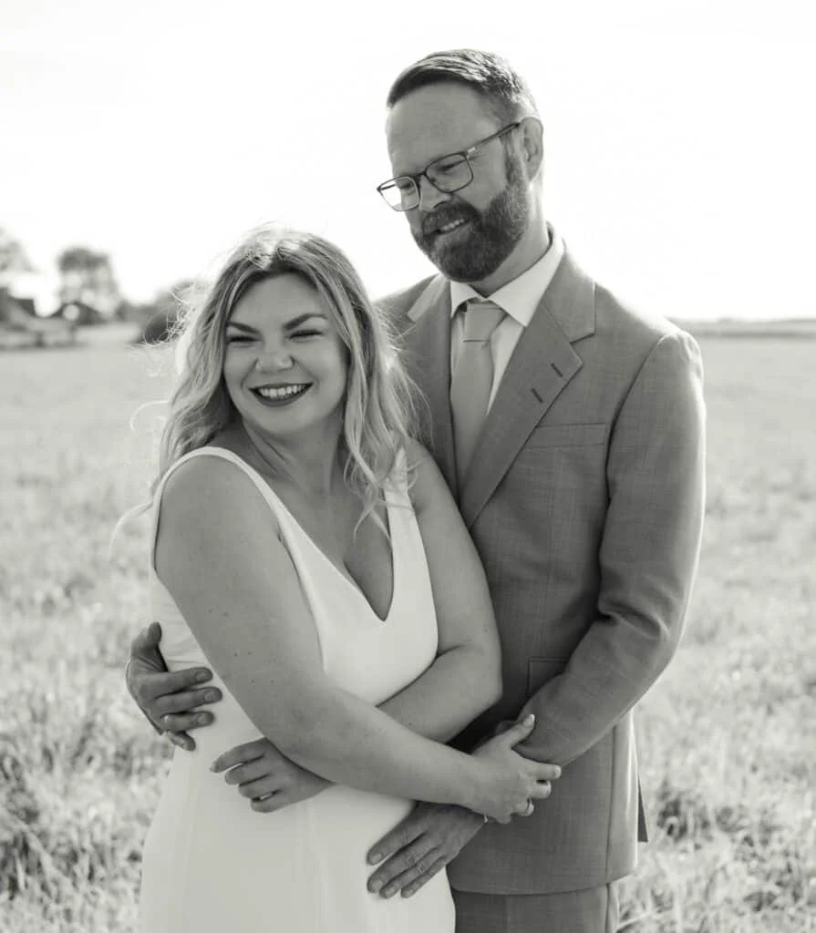 Lykkelig brudepar i sort-hvitt som holder rundt hverandre på et jorde, et vakkert minne fra profesjonell bryllups- og familie-fotografering.