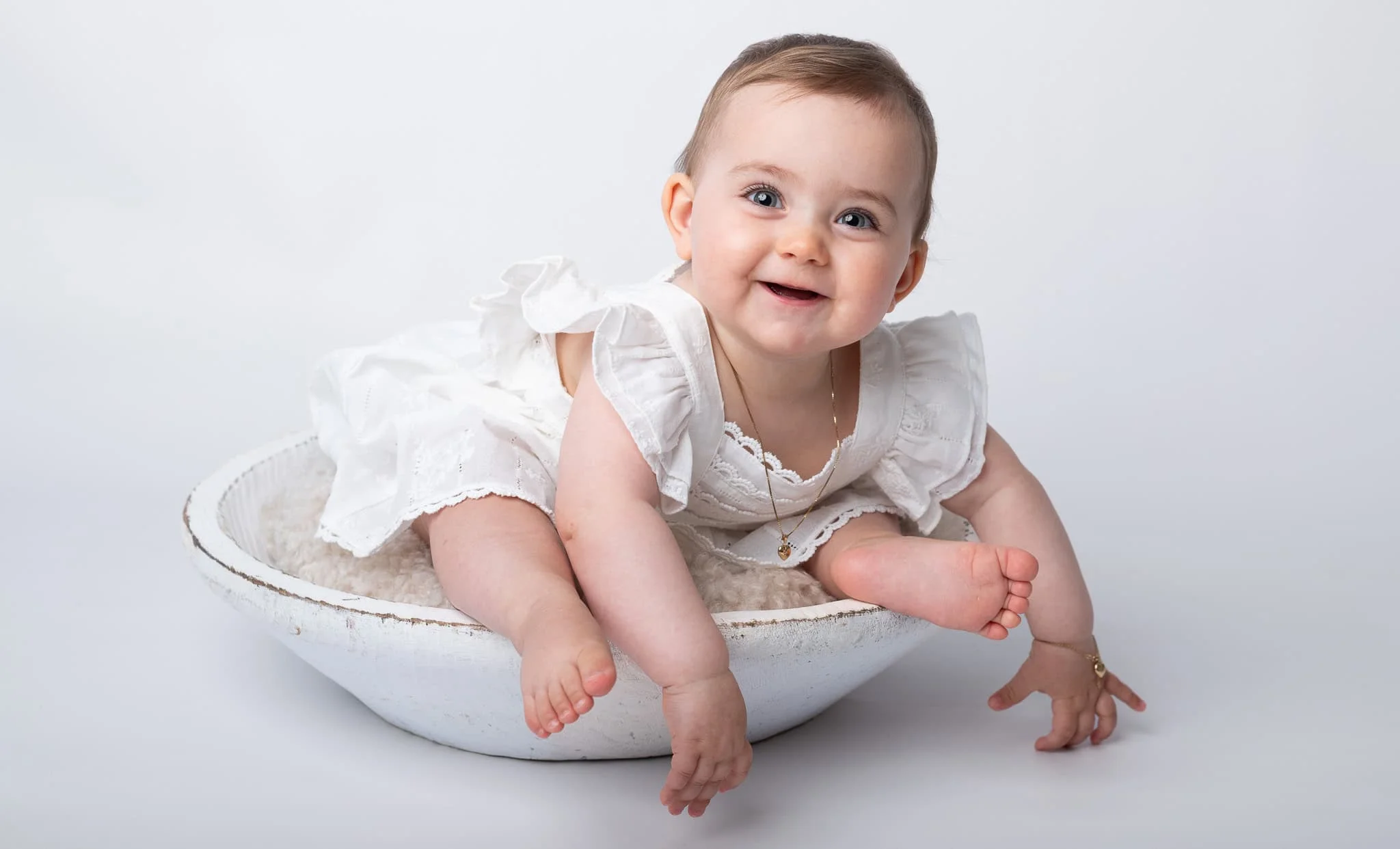 Søt baby som ligger i en hvit keramisk skål, smilende og glad.