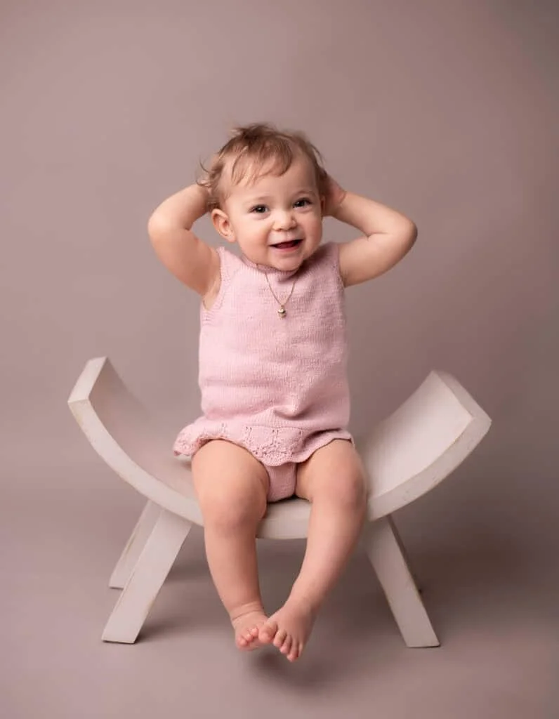 Barnefotografering av smilende liten jente i rosa klær, sittende på unik fotostol.