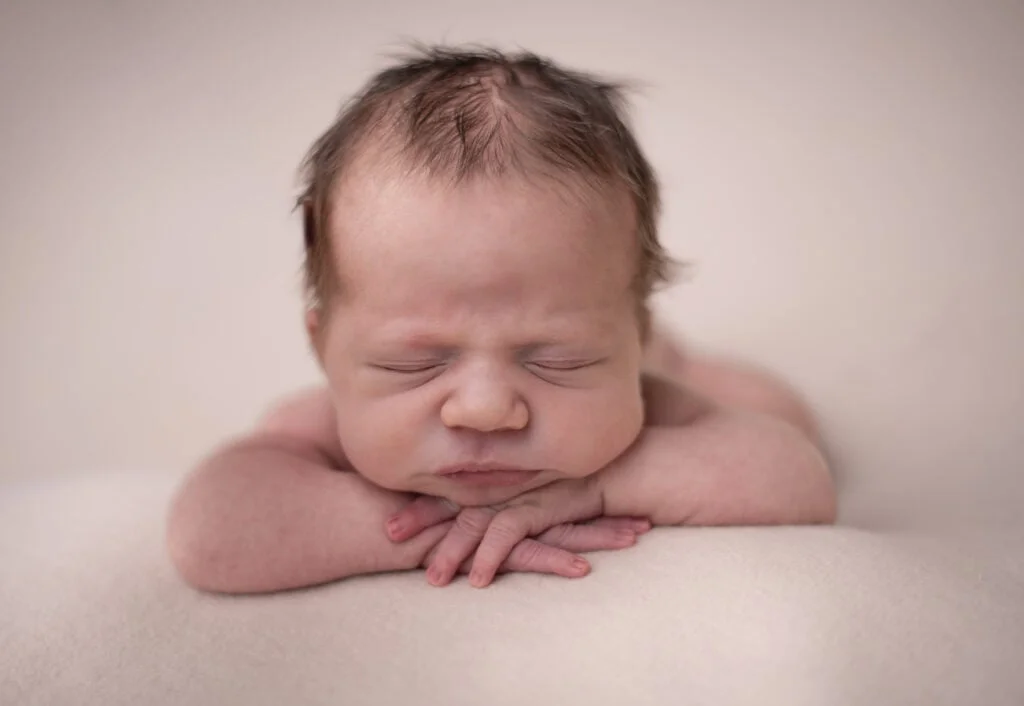 En nyfødt baby hviler med hendene under haken i en rolig fotografering.