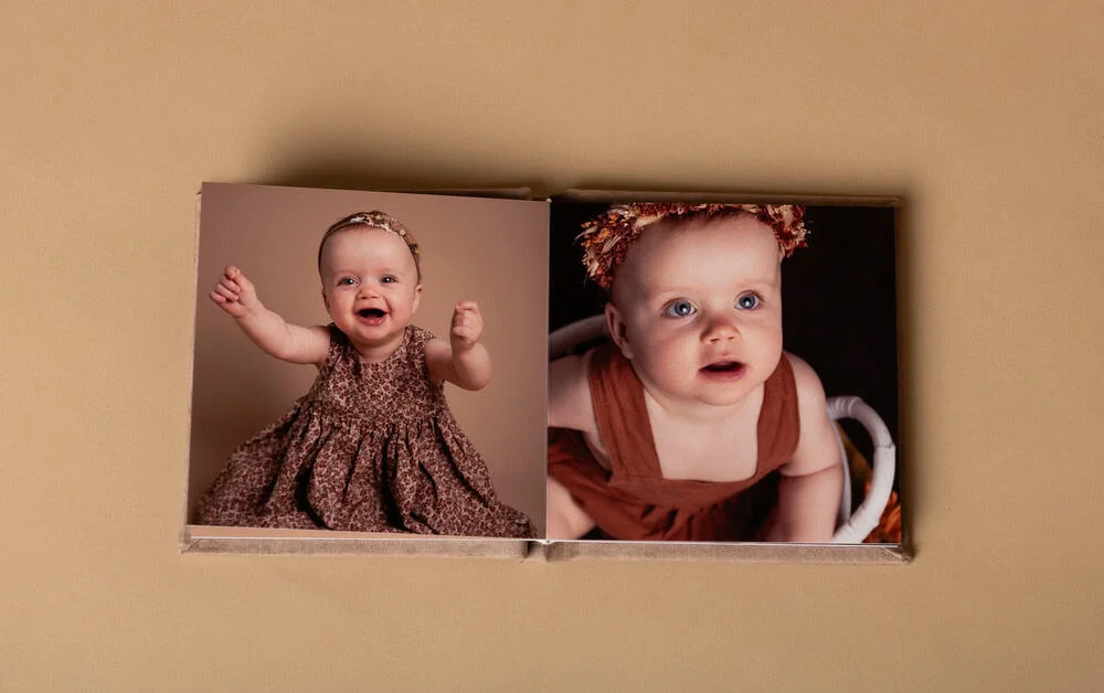 Oppslått album fra profesjonell nyfødtfotografering i fotostudio viser to bilder av en glad baby med blomsterkrans og kjole.