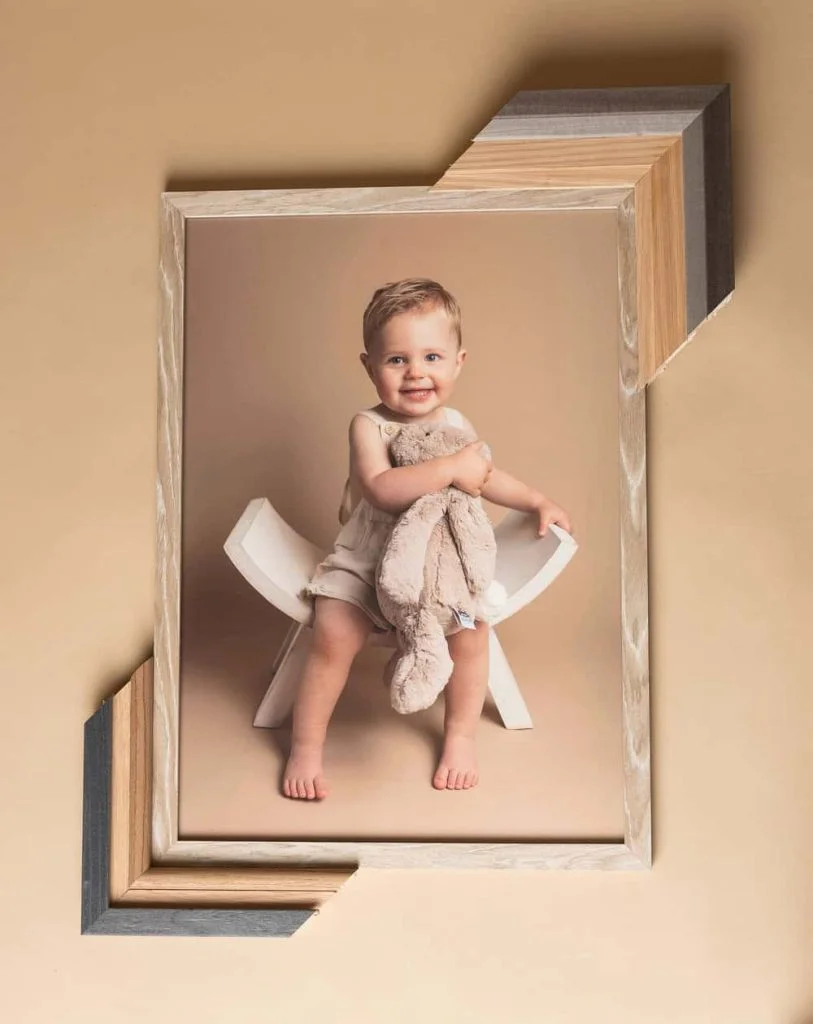 Smilende barn sitter på en hvit stol i vårt fotostudio, holder en kosedyrkanin, presentert i en stilig treramme.